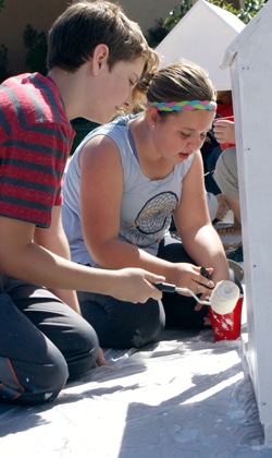two students working on painting a doghouse
