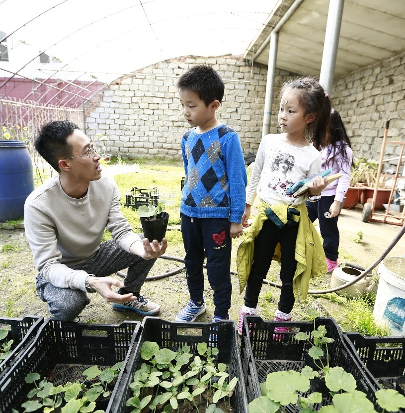 A teacher talks to two students about plants, with crates full of small plants in the foreground. 