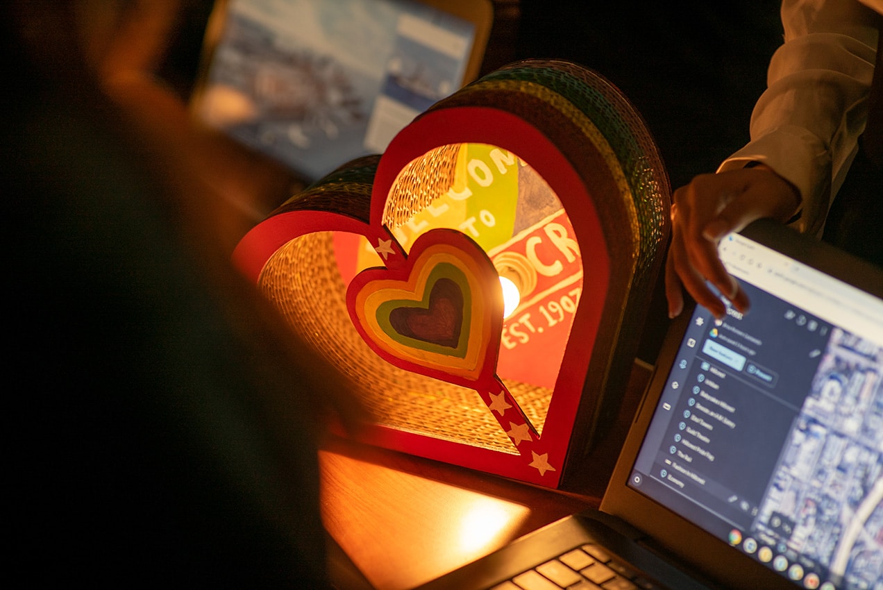 A glowing, heart-shaped student project lantern alongside a laptop screen