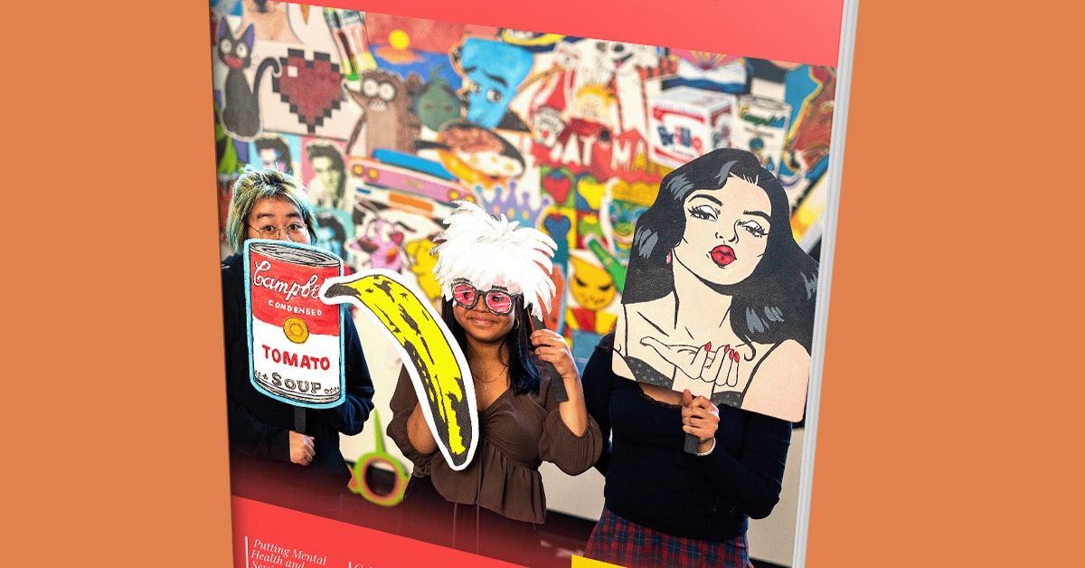 Three people hold oversized pop art props—a tomato soup can, banana, and womans face—against a vibrant, graffiti-style backdrop. This striking scene captures the bold creativity of Fall 2022, as featured in Issue 23.