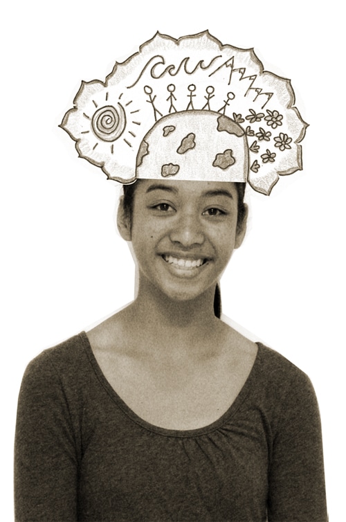 A girl smiling stands with a hand-drawn illustration of a hat on her head. The hat features doodles of the sun, flowers, people holding hands, and clouds against a backdrop of mountains. The image is in sepia tone.