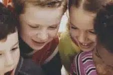 A group of children gathered closely together, smiling and looking at something in front of them. They appear engaged and happy.