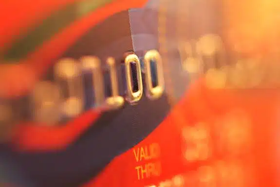 Close-up of a credit card showing embossed numbers and part of a valid thru date. The card is lit with a warm, blurred orange and red background.