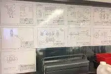 Blueprints and technical drawings are displayed on a wall, showcasing the meticulous planning needed for this campaign. A toolbox sits below them, along with a red container strategically positioned on the right.