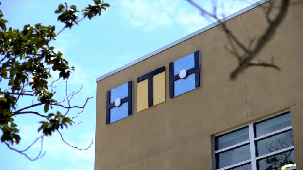 Minimalist building facade with geometric window designs in black and gold against a clear blue sky, offering an innovative aesthetic akin to the High Tech High Graduate School of Education. Surrounding branches add contrast to the modern architectural style.
