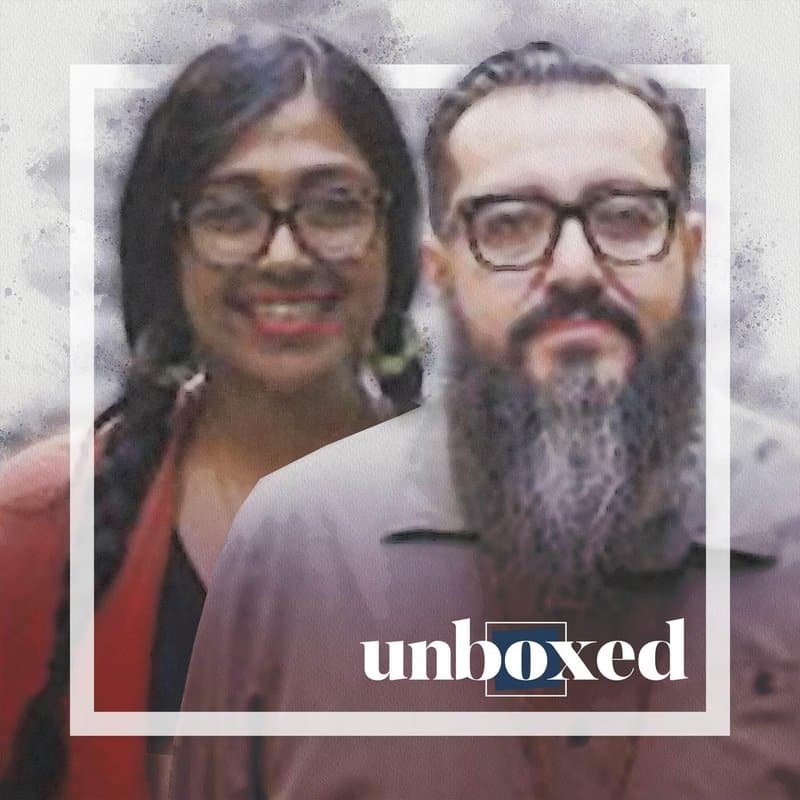 A man with a beard and glasses stands in front of a smiling woman with long hair and glasses, framed in white. The word unboxed appears near the bottom, hinting at the La Junta Collectives mission to heal trauma.