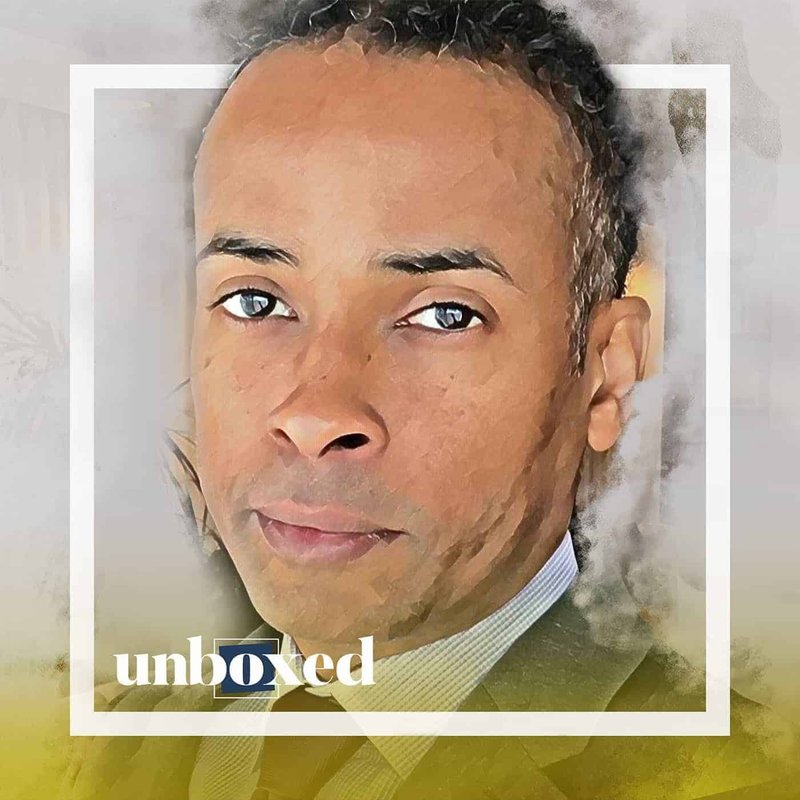 A digitally altered portrait of a man with short hair wearing a suit and tie. The image, reminiscent of LeDerick Hornes impactful advocacy, has a painted effect framed by a white border. Unboxed appears in the lower-left corner against a gradient background of gray and yellowish tones.