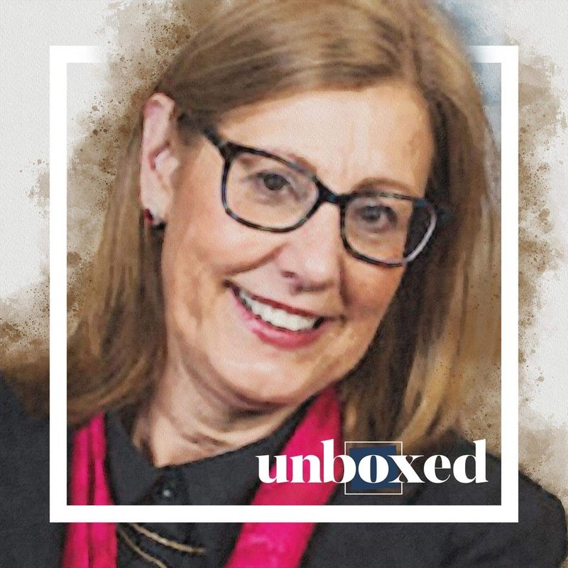 A woman with glasses and a pink scarf smiles warmly, embodying the essence of online learning. The image is framed with a white border, showcasing the word unboxed in the corner. Dr. Margo Vreeburg Izzos influence is subtly reflected in the soft, textured blend of colors in the background.