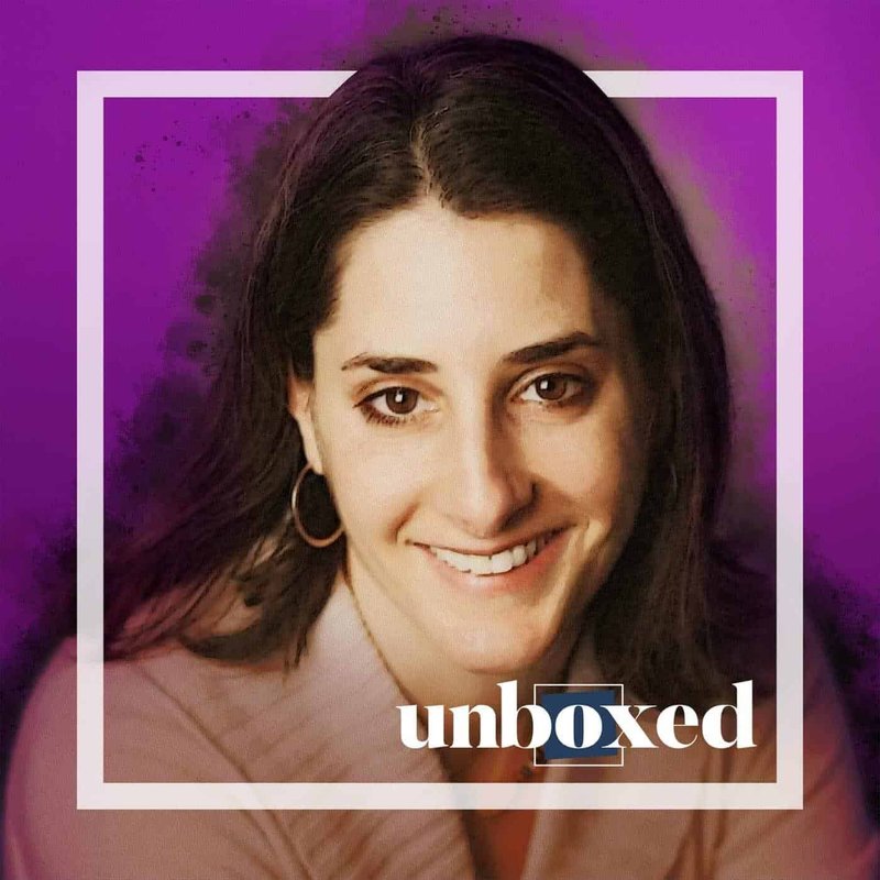A person with long brown hair and hoop earrings smiles at the camera against a purple backdrop, embodying the essence of meaning-making. The words unboxed appear subtly at the bottom.