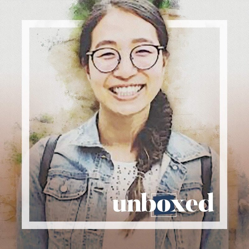 A person with long hair and glasses smiles brightly, wearing a denim jacket and carrying a backpack, banishing awkward silence. The word unboxed appears at the bottom. The image has a watercolor effect with a modern frame.