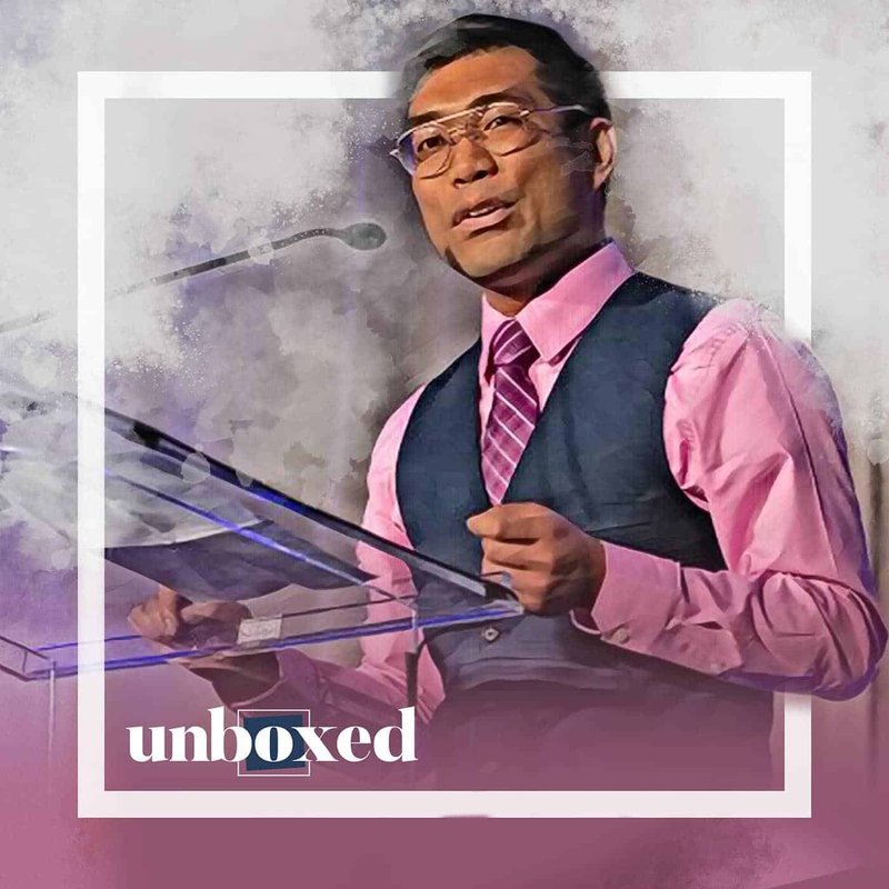 A man in a pink shirt, purple tie, and blue vest speaks at a podium with a microphone. The background is a textured blend of white and purple. The word unboxed is displayed in the corner as Rick Oculto delivers his message on supporting LGBTQ+ youth.