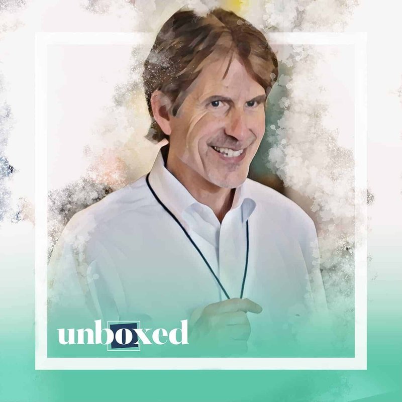 A smiling man with brown hair wears a white shirt and a lanyard. The image boasts a watercolor effect and pastel green gradient at the bottom, featuring unboxed in white text. Its reminiscent of Ron Berger’s beautiful lessons, capturing inspiration in every brushstroke.