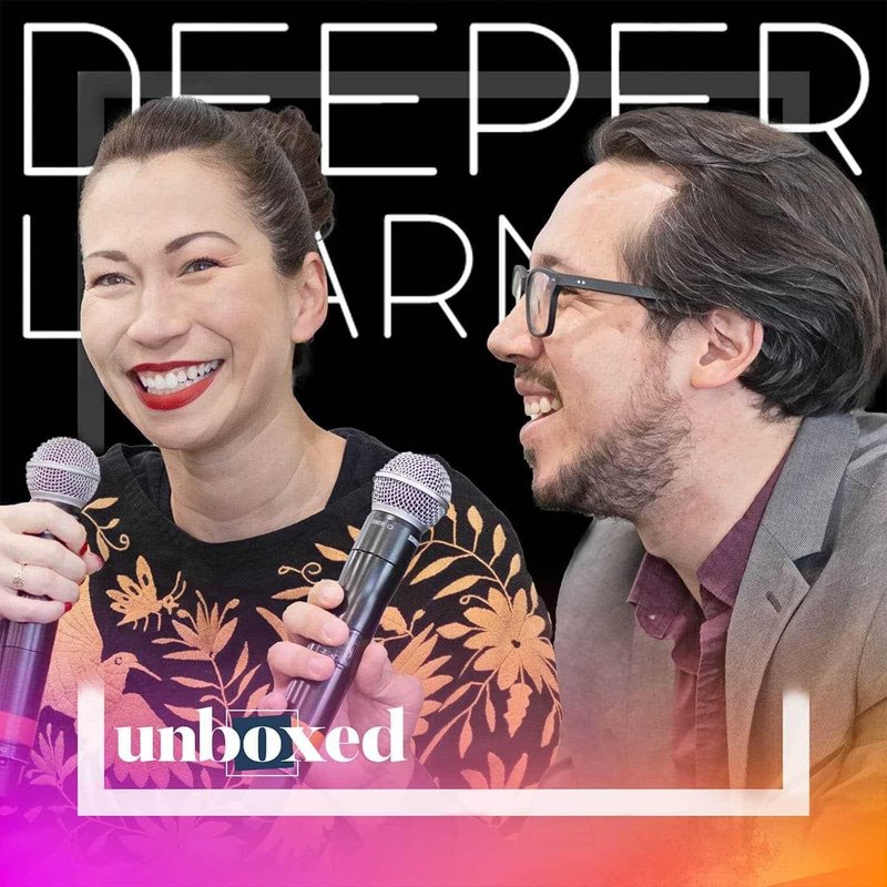 A woman and a man from Freedom University are smiling and talking while holding microphones. The background features the words Deeper Learning. A colorful graphic at the bottom reads unboxed. The woman wears a floral top, and the man is in a suit and glasses.