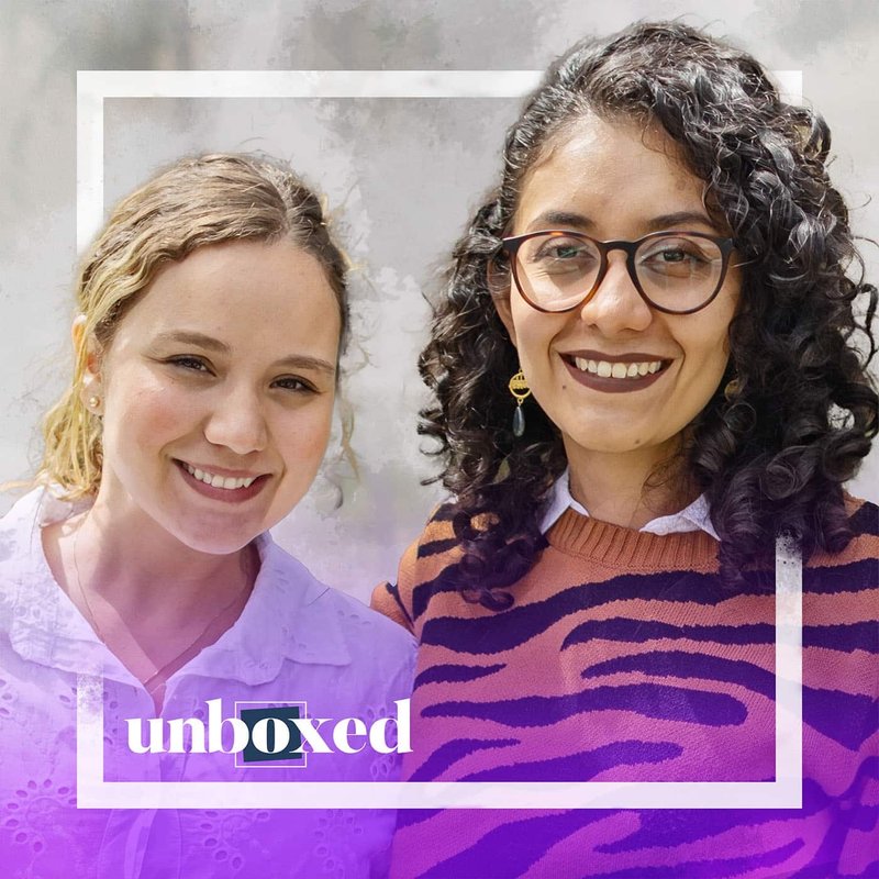 Two smiling women stand side by side. The woman on the left wears a white blouse, and the one on the right wears glasses and a patterned sweater. A digital frame surrounds them with unboxed at the bottom, perhaps showcasing their connection to progressive ideas like Neuroscience or Cosmo Schools.