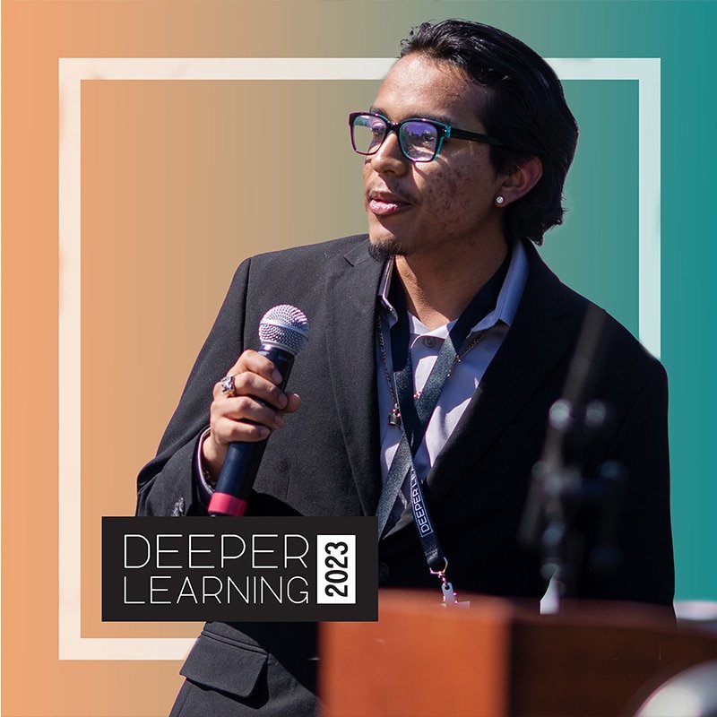 Walter Cortina, founder of Bridgemakers, speaks at a podium in a suit and glasses, gripping the microphone confidently. Behind him, a gradient of orange to teal sets the stage with Deeper Learning 2023 boldly displayed in a black square.