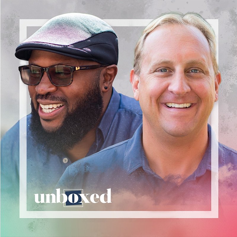 Two smiling men in casual shirts are framed by a colorful gradient border with the word unboxed in the lower left corner. One man wears glasses and a hat, while the other has short hair. Their cheerful demeanor captures the spirit of radicals who get stuff done with creativity and flair.