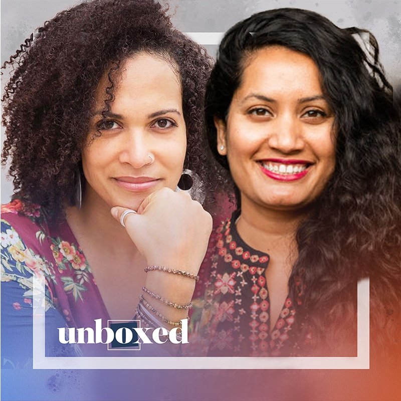 Two women are smiling, side by side, embodying a sense of community. The woman on the left has curly hair and rests her chin on her hand, adorned in a floral top. Her friend, with long wavy hair, wears a patterned blouse. The word unboxed is in the corner.