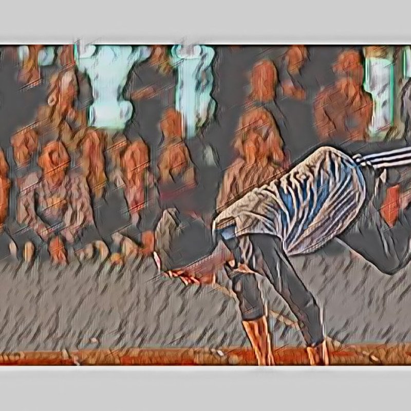 A stylized image of a breakdancer performing a one-handed freeze at the Breaks Exhibition. The dancer wears a cap, a striped shirt, and track pants. An audience in soft focus watches in the background. The image has an artistic, painted effect.