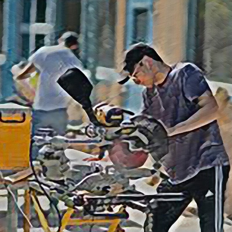 A person wearing a cap operates a power tool, possibly a saw, in an outdoor setting, showcasing high design principles. Another person is blurred in the background, working near a wooden structure. The image has a painterly effect.