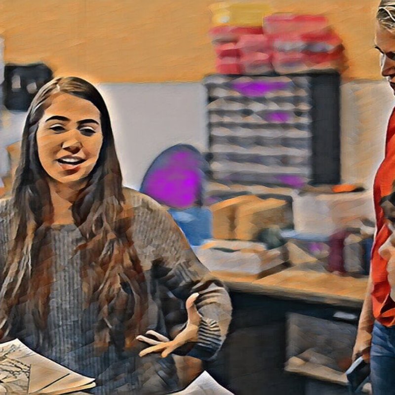 A digitally altered image shows a woman with long hair talking energetically about the importance of collaboration next to two people. They are indoors, surrounded by shelves and supplies, creating an informal, workshop feel where the value of critique can truly be appreciated.
