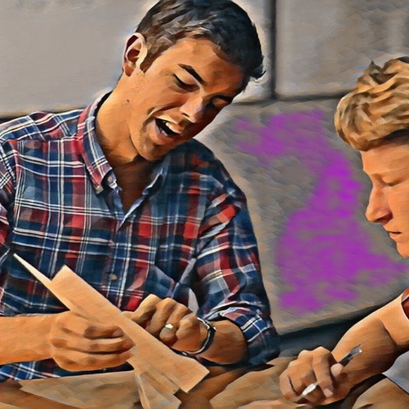 Two people sit at a table, one enthusiastically discussing the importance of revision while holding a paper. Both sport plaid shirts, and the muted colors in the background create a friendly, collaborative atmosphere.