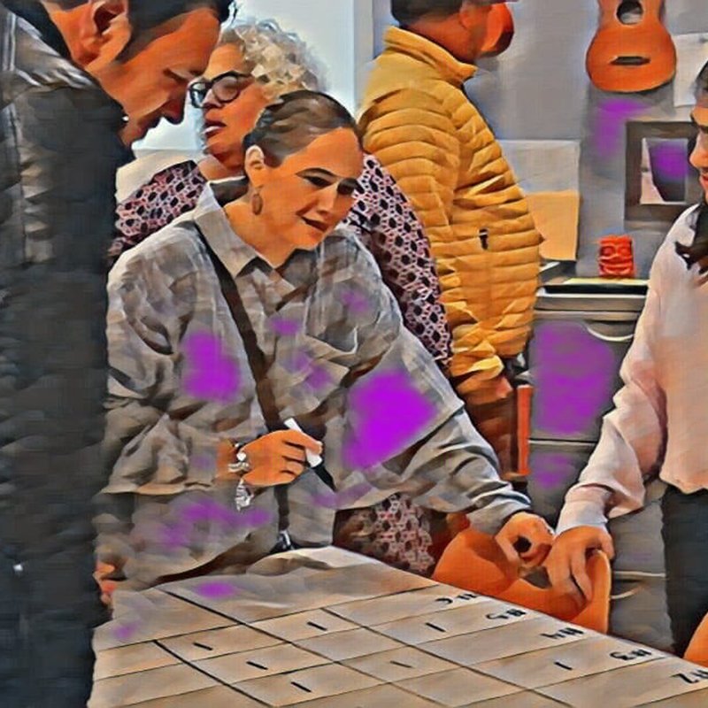 A group of people gathered around a table, with one woman pointing at a grid on paper. Theyre in a room with vibrant walls and a guitar on the wall, reminiscent of an art exhibition. The atmosphere blends casual engagement with an air of truthiness as they explore ideas together.