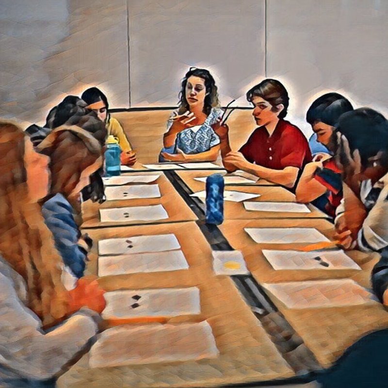 A group of people sits around a long table with papers in front of them, engaged in discussion. The setting resembles a Project Tuning Protocol meeting, where optimization is key. The image is stylized with an artistic filter, capturing the essence of project management finesse.