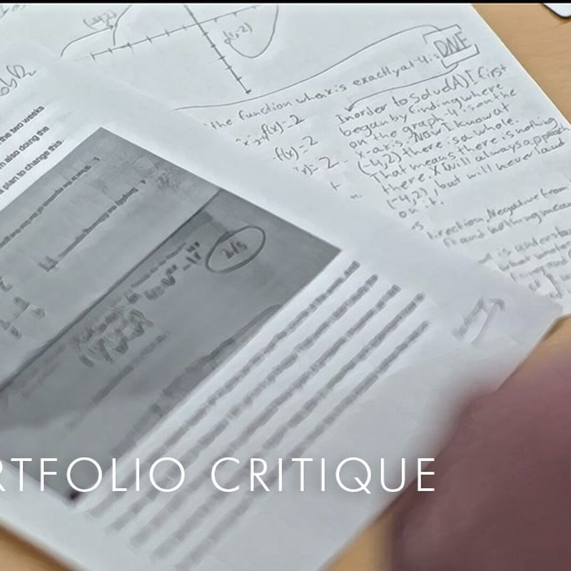 A table with handwritten notes and a printed document, showcasing a math portfolio. A partially visible hand suggests a critique is underway. Text overlay reads PORTFOLIO CRITIQUE, with the focus on mathematical functions and written feedback.