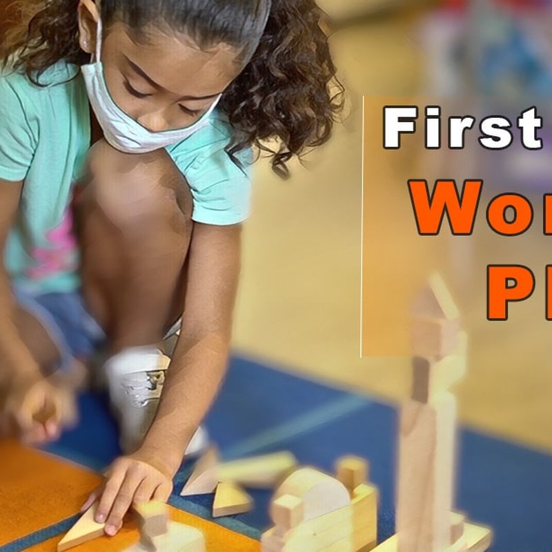 A young girl in a mask is immersed in playful learning, arranging wooden building blocks on the floor. Her focus embodies the concept of Work in Play. The text First... Working PL hints at her educational journey toward first grade.