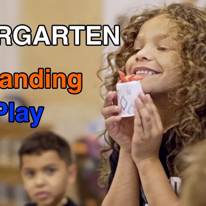 A child in a classroom smiles while holding a small craft item. The bold words Kindergarten: Expanding Play and Understanding are displayed prominently. In the background, other children are present, engaged in cheerful exploration.