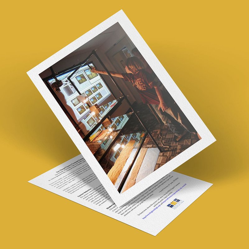 A tilted photograph of a person reaching toward a glass display case in a room with large windows rests on a yellow surface. Overlapping this scene is the notion of Crossed Gazes, as if bridging perspectives between San Diego and Tijuana. The photo sits atop a sheet of paper with text and logos, slightly bent upward.