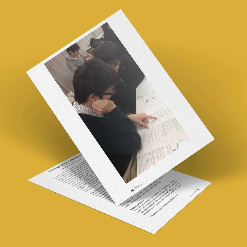Two men are seated and reviewing documents in a meeting room, one pointing at a page. The scene, reminiscent of an English playtesting session, is captured on a paper cutout with a yellow background.