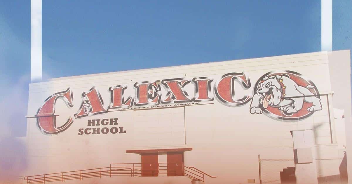 The Calexico High School building proudly displays a large sign with its bulldog mascot. Under a clear blue sky, the white structure stands as a symbol of community spirit and academic dedication, encouraging students to achieve milestones like FAFSA completion.