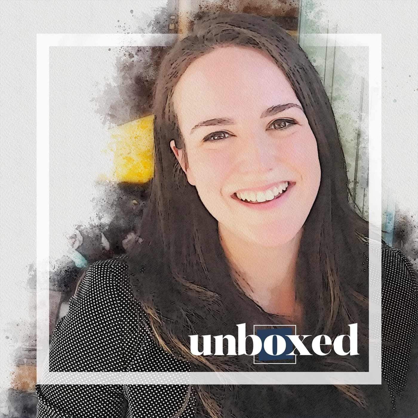 A person with long dark hair is smiling at the camera, radiating positivity. The image, framed with a watercolor effect and white border, features the word unboxed. This portrait subtly highlights the importance of mental health and supporting well-being in every aspect.