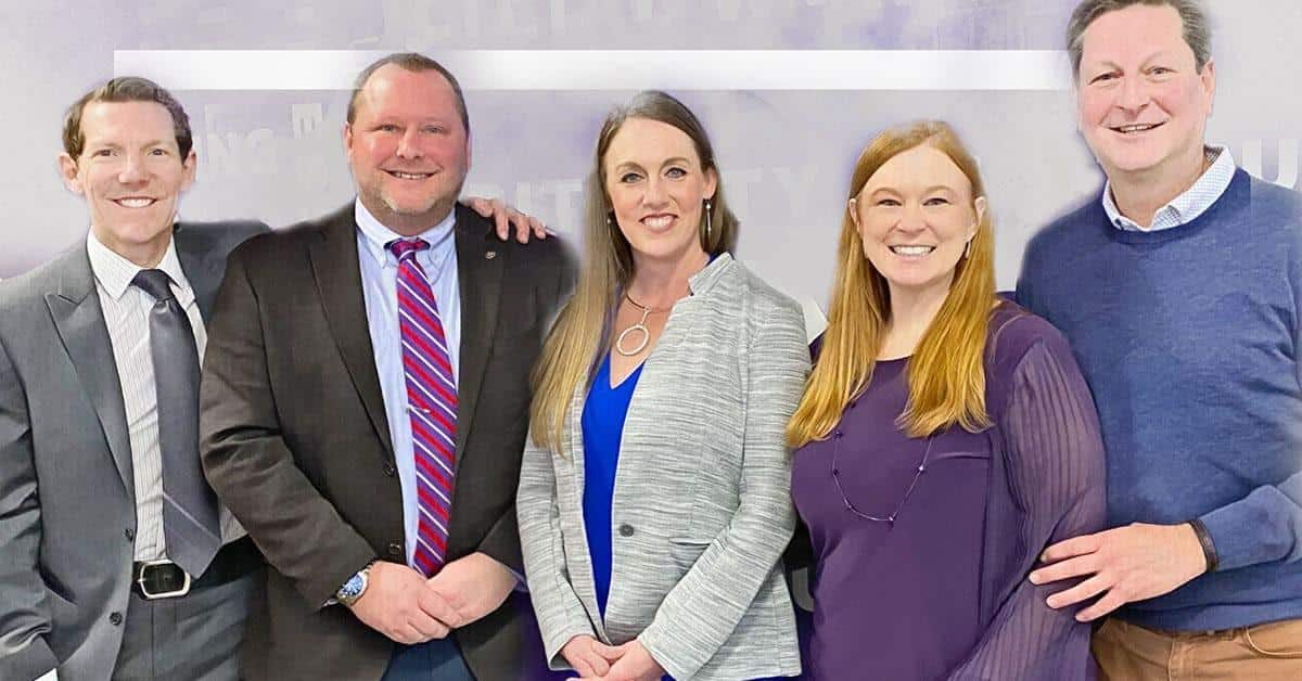 Five people stand together, smiling, their Doctorates in Education a testament to their dedication. The group consists of three men and two women, dressed in a mix of business and casual attire. The neutral, blurred background emphasizes their commitment to improved education.