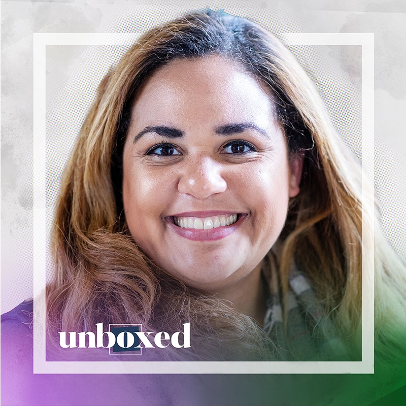 A person with long hair smiling at the camera, framed by a square border with a pink and green gradient. The word unboxed is at the bottom, partially highlighted. Its as if Jillian Juman herself beckons deeper learning beyond the frame.