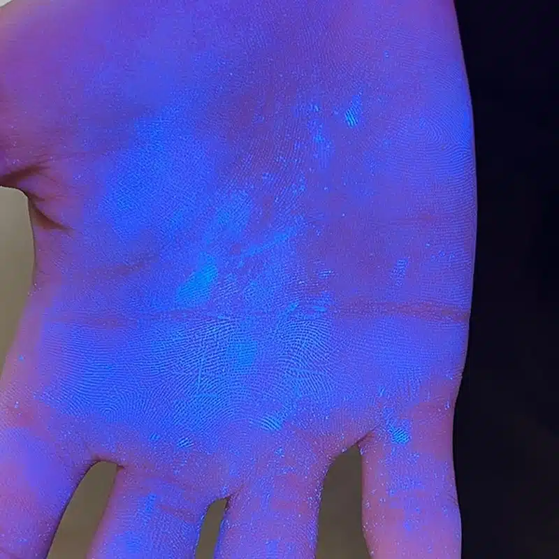 A close-up of a hand under UV light reveals glowing blue particles scattered across the skin, highlighting fingerprints and texture—a striking visual that perfectly captures the curiosity-driven spirit of Small-ologies within the Honors Pathways program.
