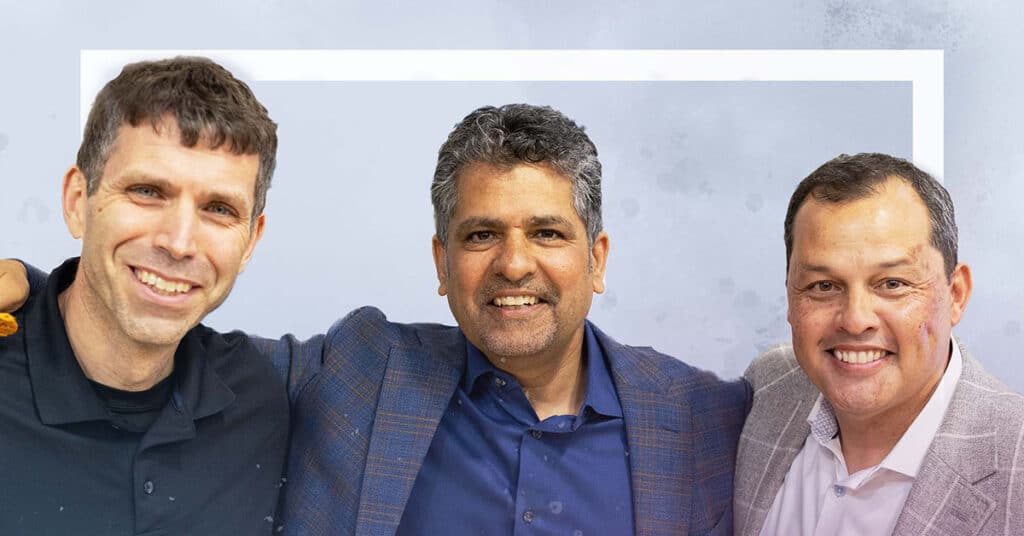 Three men are standing side by side, smiling at the camera. Their expressions reflect a spirit of deeper learning and continuous improvement, with the man on the left in a black shirt, the middle in blue, and the right in a light-colored jacket.