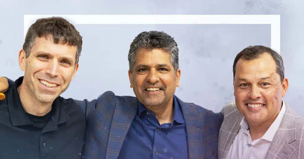 Three men are standing side by side, smiling at the camera. Their expressions reflect a spirit of deeper learning and continuous improvement, with the man on the left in a black shirt, the middle in blue, and the right in a light-colored jacket.