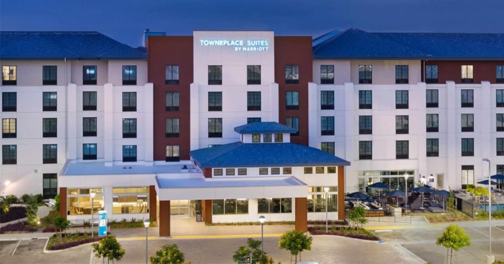 Front view of TownePlace Suites by Marriott hotel at night, with illuminated sign and modern exterior. Large windows overlook an outdoor seating area, creating a welcoming environment perfect for Deeper Learning discussions or Deeper Learning 2026 events.