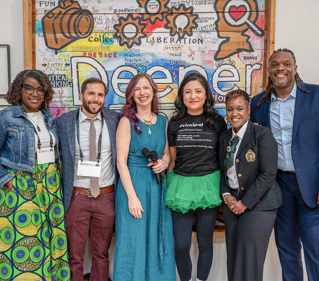 Six people smile together in front of a colorful mural with words like liberation, empathy, and think. One holds microphones, sporting bright, professional, and casual clothes—capturing the collaborative spirit of a BIG Event Template.