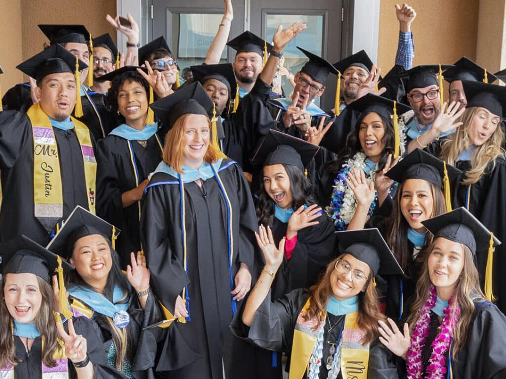 A group of diverse graduates in caps and gowns smiles and cheers enthusiastically while posing together, celebrating their achievement outside a building—ready to take the next step with our Credential & Degree Programs: Interest form.