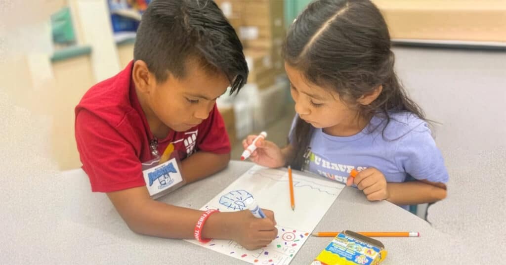 Two young children sit at a table, drawing together with markers as art supplies scatter around—illustrating how DEEP San Diego fosters creativity and helps solve literacy challenges from an early age.