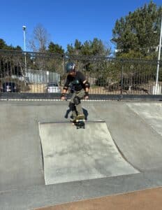 A person wearing a helmet and pads is skateboarding down a ramp at an outdoor skatepark on a sunny day, surrounded by trees and a fence—capturing the adventurous spirit featured in Unboxed Issue 29.