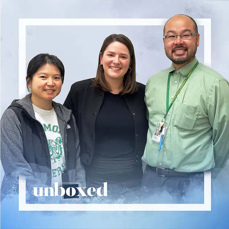 Three people stand side by side, smiling at the camera. The left person wears a gray jacket, the middle person wears black, and the right—wearing a green shirt with an ID badge from Fremont High School. The word unboxed appears at the bottom.