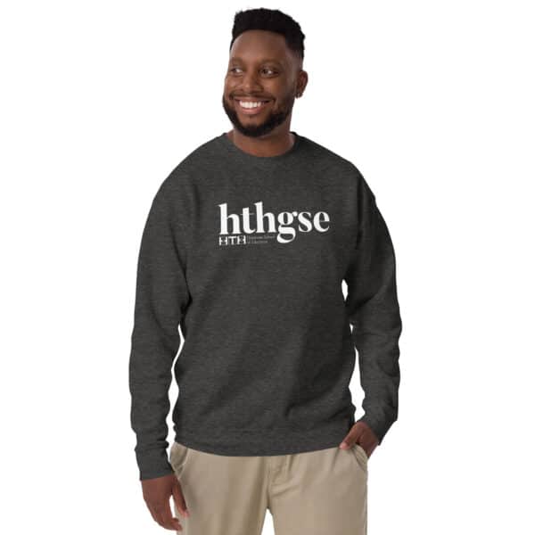 A smiling man with a beard wears a dark gray Unisex Crew Neck Sweatshirt featuring "hthgse" and smaller white text on the front. He stands with one hand in his pocket against a plain white background.