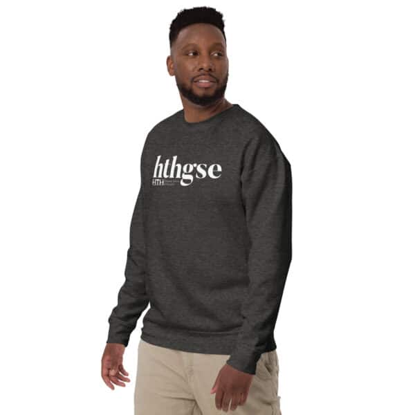 A man in a dark gray Unisex Crew Neck Sweatshirt with a bold white logo on the front stands facing slightly to the side, paired with light khaki pants against a plain white background.