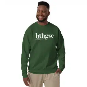 A smiling man with short hair and a beard wears a unisex crew neck sweatshirt, featuring “hthgse” in large white letters on the front. He stands against a plain white background with one hand in his pocket.