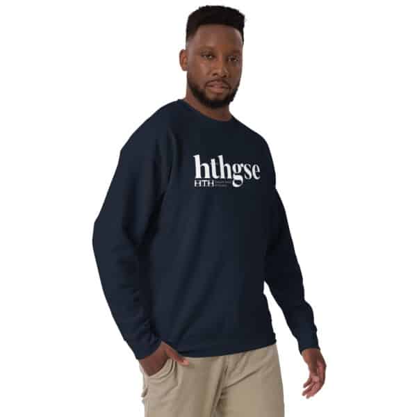 A man with a trimmed beard wears a navy blue Unisex Crew Neck Sweatshirt with a white logo, "hthgse," printed on the front. He stands facing slightly sideways, one hand relaxed at his side, paired with khaki pants against a white background.