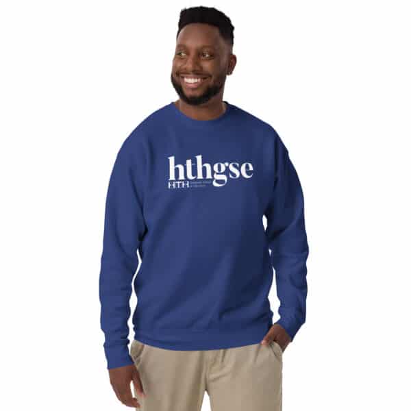 A smiling man in a unisex crew neck sweatshirt, royal blue with a bold white logo reading hthgse, and khaki pants stands against a white background.